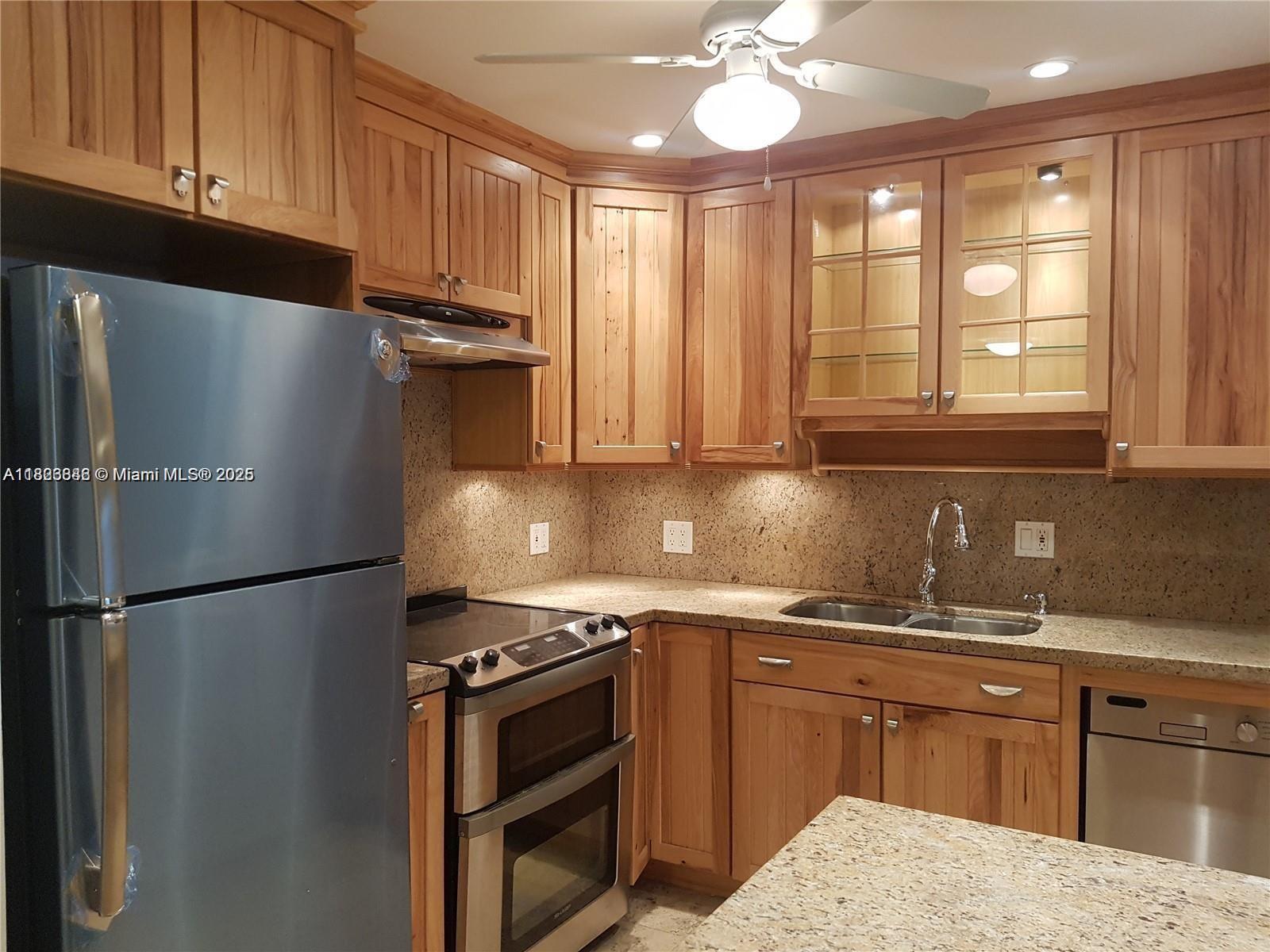 A kitchen features wooden cabinets, stainless steel appliances, and speckled granite countertops — 253 S Cypress Rd # 237, Pompano Beach FL 33060, POMPANO BEACH, FL