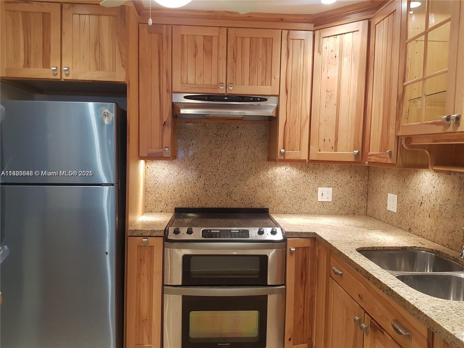 A kitchen features wood cabinets, stainless steel appliances, and speckled granite countertops — 253 S Cypress Rd # 237, Pompano Beach FL 33060, POMPANO BEACH, FL