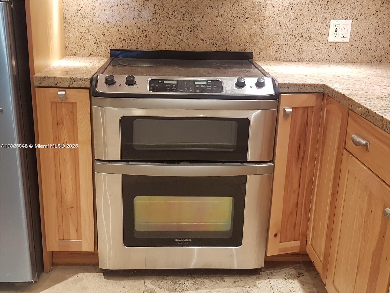 A stainless steel double oven range is situated between wooden cabinets and granite countertops — 253 S Cypress Rd # 237, Pompano Beach FL 33060, POMPANO BEACH, FL