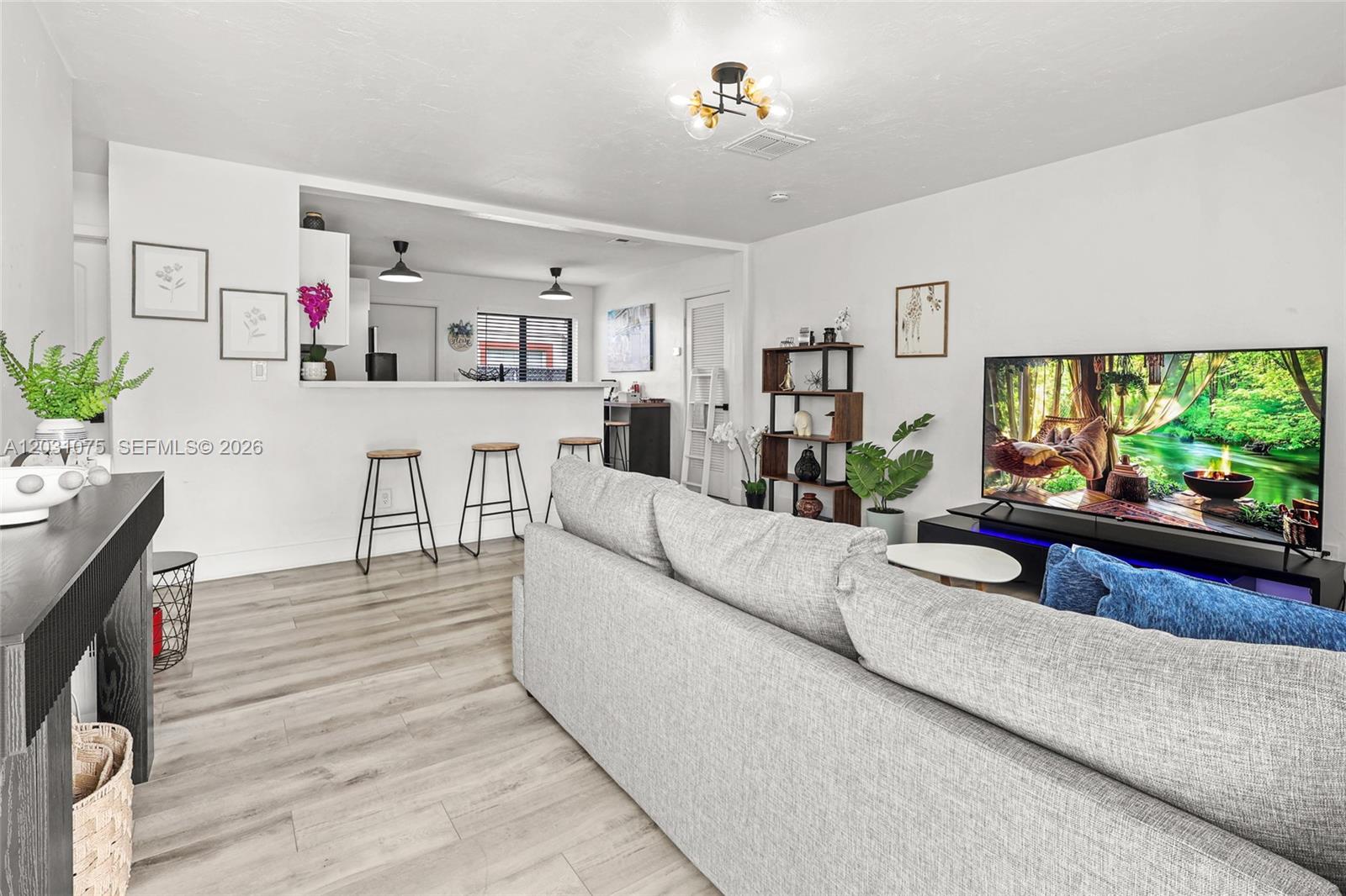 A living room with light wood-look flooring features a gray sofa and a television — 11002 NE 13th Ave, Miami FL 33161, MIAMI, FL