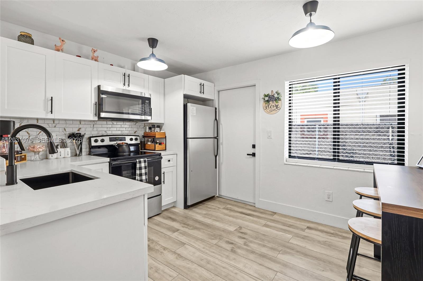 A modern kitchen features white cabinets, stainless steel appliances, quartz countertops, and wood-look flooring — 11002 NE 13th Ave, Miami FL 33161, MIAMI, FL