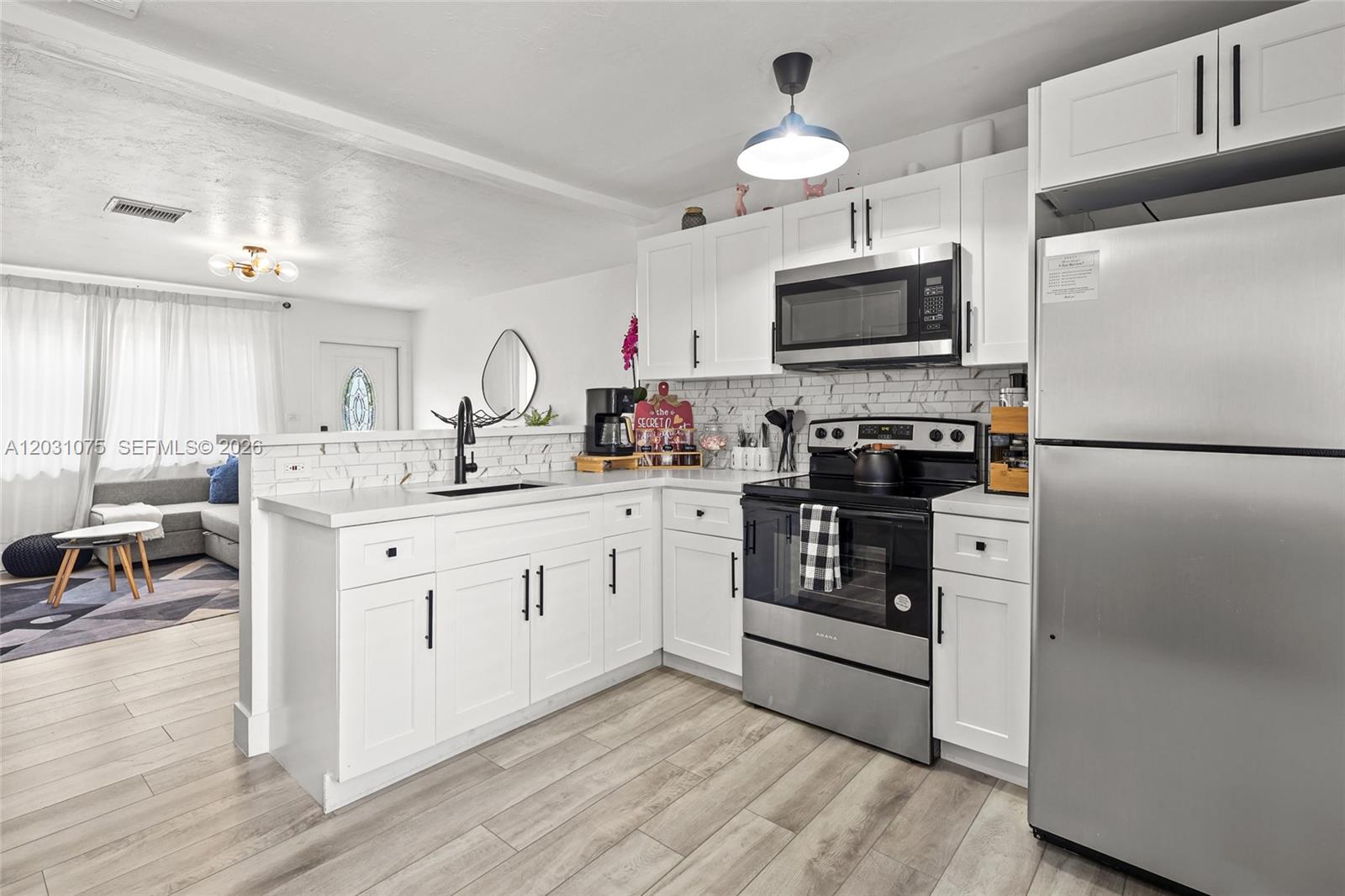 A modern kitchen features white cabinets, stainless steel appliances, and a marble-patterned backsplash — 11002 NE 13th Ave, Miami FL 33161, MIAMI, FL