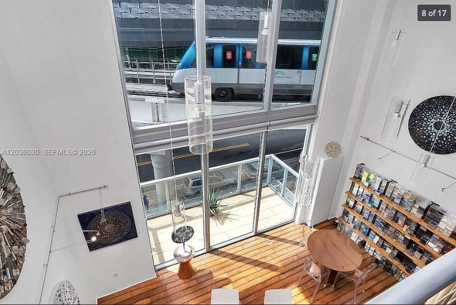 A high-ceilinged living area features wood floors, a dining set, and a view of a train — 1050 Brickell Ave # 208, Miami FL 33131, MIAMI, FL
