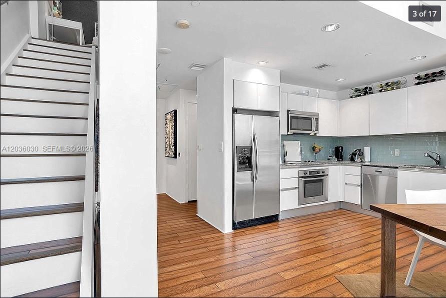 A kitchen with white cabinets, stainless steel appliances, and wood flooring next to a staircase — 1050 Brickell Ave # 208, Miami FL 33131, MIAMI, FL