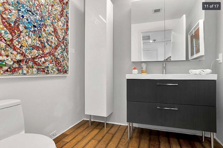 A modern bathroom features a dark wood vanity, a tall white cabinet, and colorful wall art — 1050 Brickell Ave # 208, Miami FL 33131, MIAMI, FL