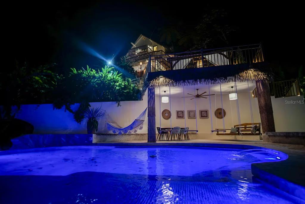 A swimming pool sits in front of a covered patio with hanging swings at night — CALLE 9 Mameyes II COLINAS DEL YUNQUE UNIT 19 I, RIO GRANDE, PR