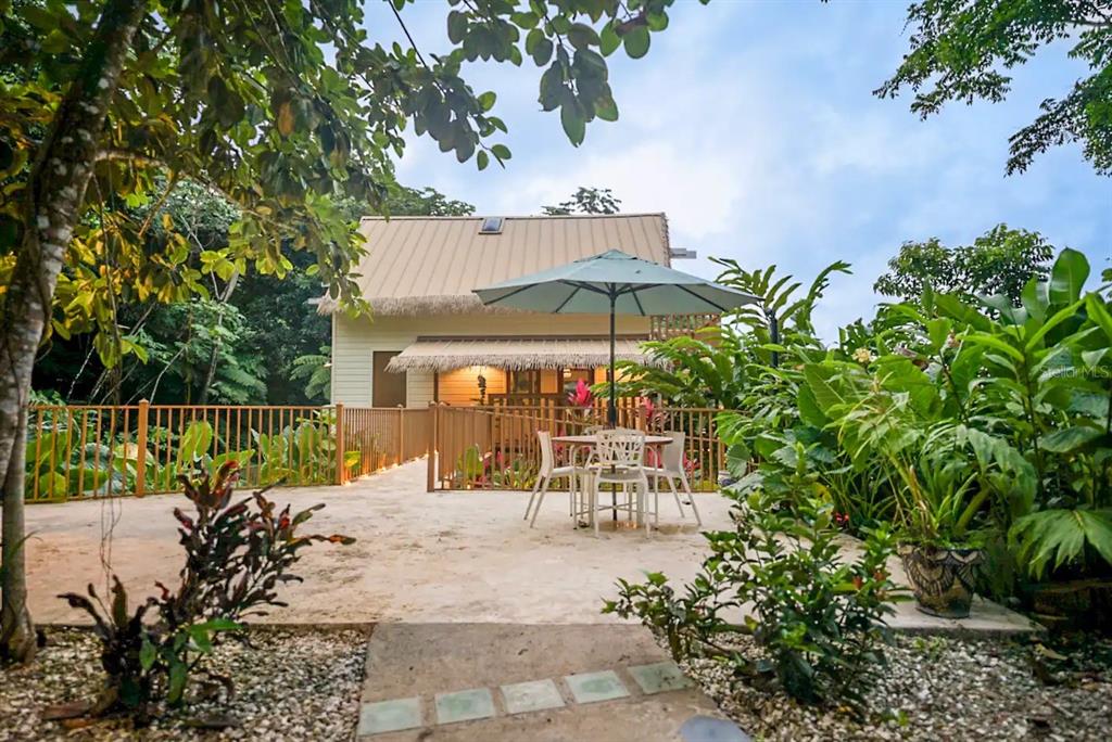 A patio with a dining set and umbrella sits in front of a small house — CALLE 9 Mameyes II COLINAS DEL YUNQUE UNIT 19 I, RIO GRANDE, PR