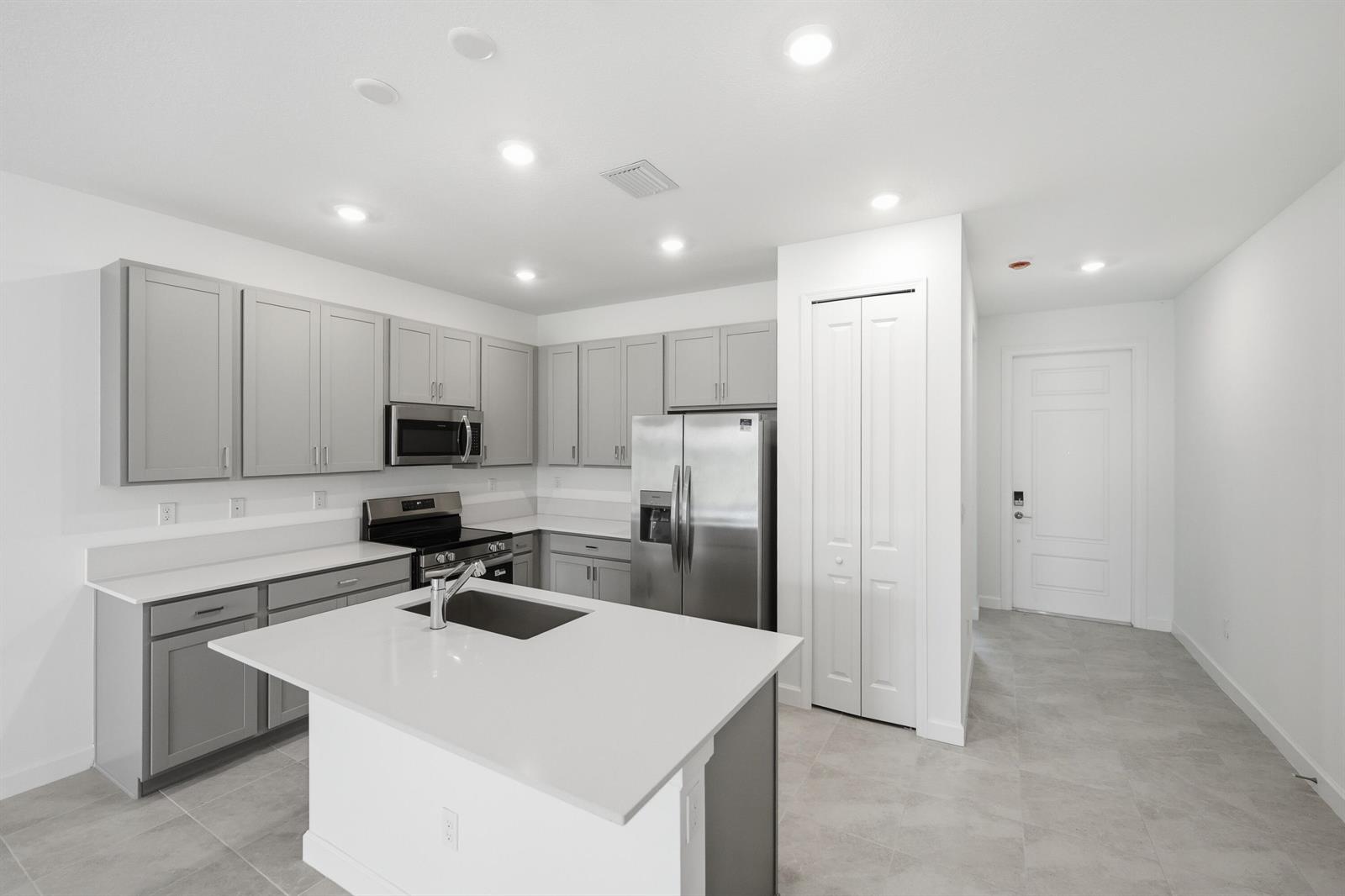 A modern kitchen features gray cabinets, stainless steel appliances, a white island, and tile flooring — 3622 Spanish Cedar Place, Fort Pierce FL 34946, FORT PIERCE, FL