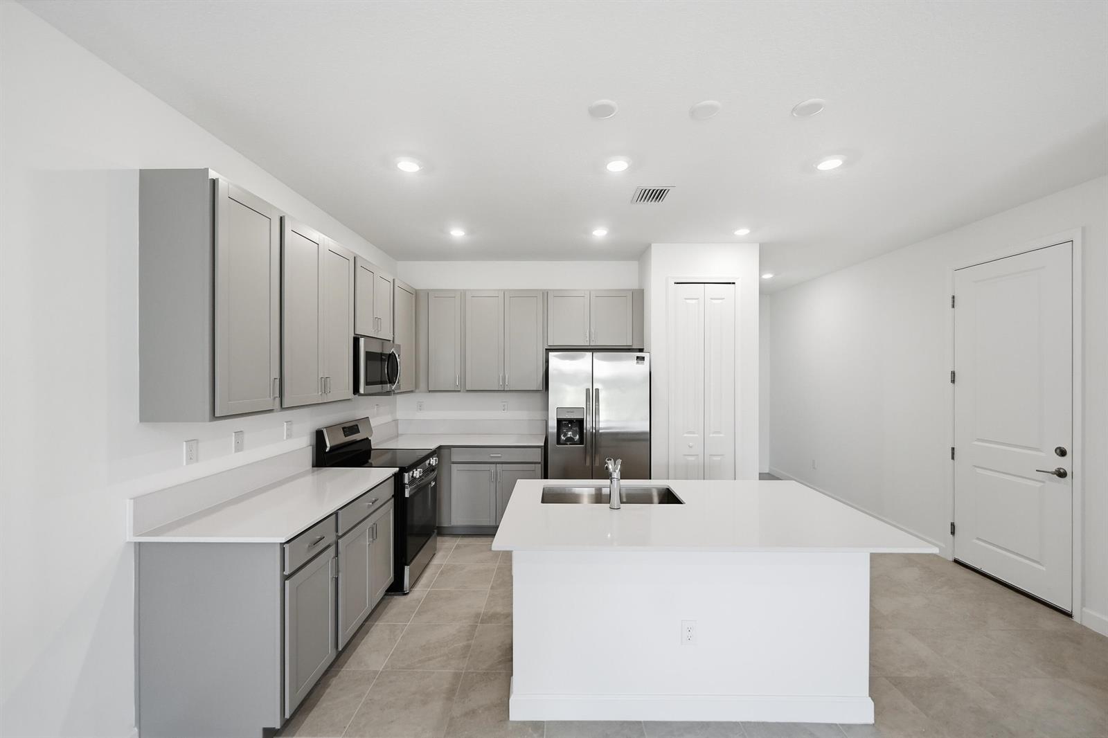 A modern kitchen features gray cabinets, white countertops, stainless steel appliances, and a central island — 3622 Spanish Cedar Place, Fort Pierce FL 34946, FORT PIERCE, FL