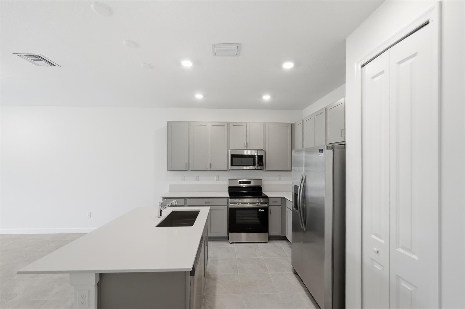 A modern kitchen features gray cabinets, stainless steel appliances, a white island, and tile flooring — 3622 Spanish Cedar Place, Fort Pierce FL 34946, FORT PIERCE, FL