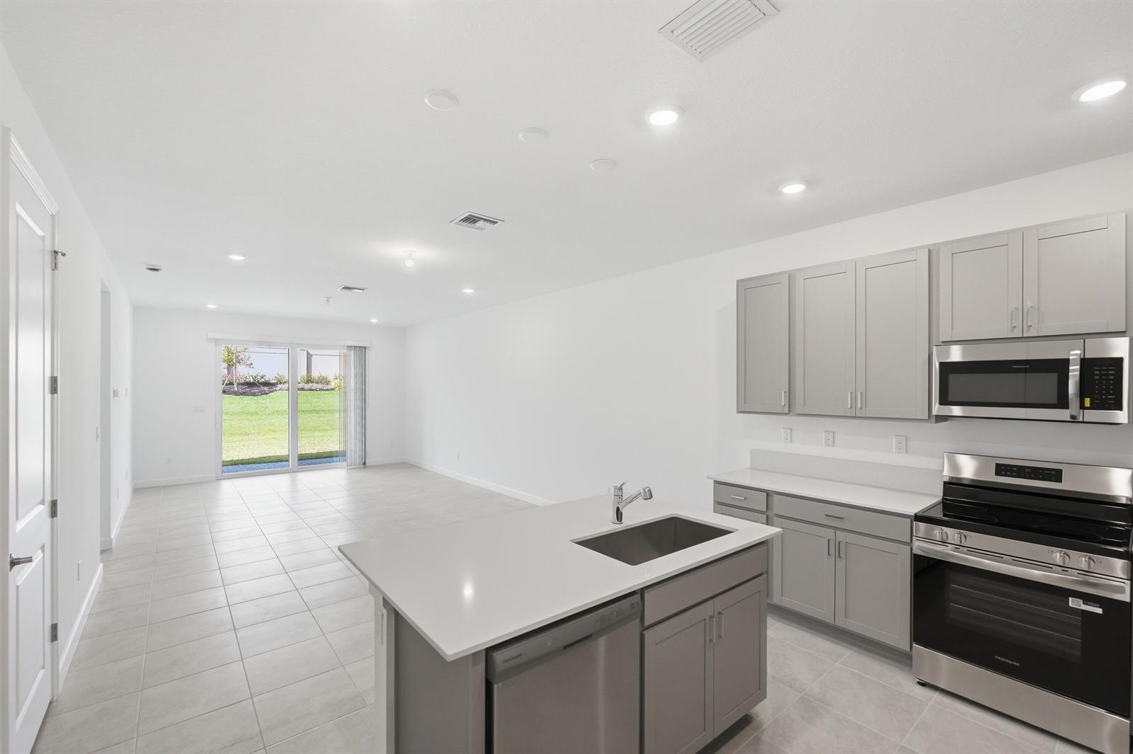 A kitchen with gray cabinets and stainless steel appliances opens to a bright living area — 3622 Spanish Cedar Place, Fort Pierce FL 34946, FORT PIERCE, FL