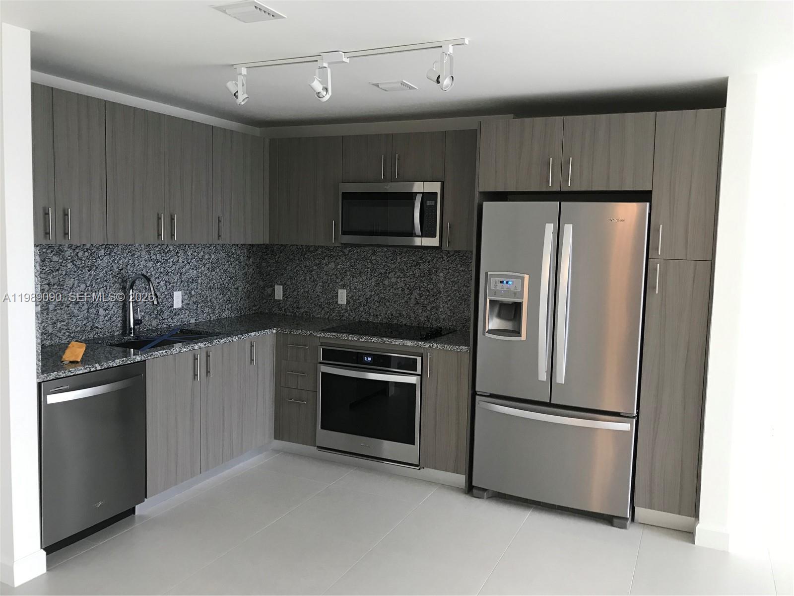 A modern kitchen features gray wood-grain cabinets, stainless steel appliances, and speckled granite countertops — 5350 NW 84th Ave # 1814, Doral FL 33166, DORAL, FL