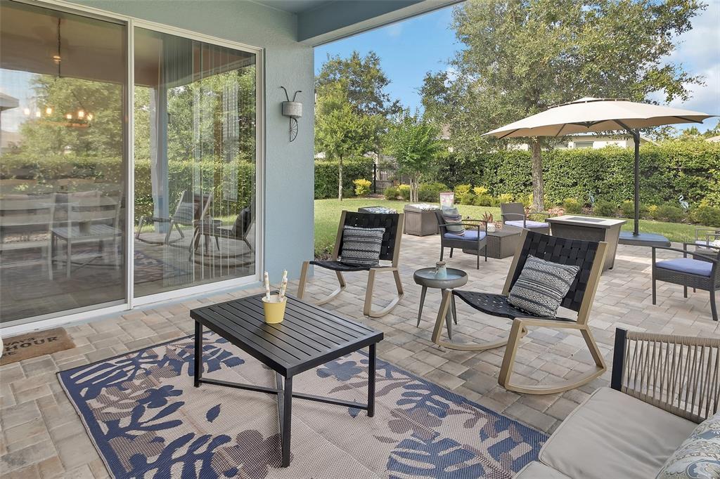 A paved patio features outdoor furniture, a rug, and a large umbrella in a backyard — 744 E VICTORIA TRAILS BOULEVARD, DELAND, FL