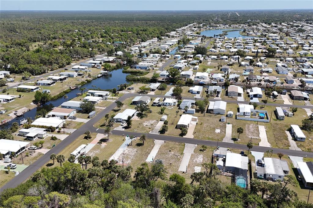 An aerial view shows a residential community with mobile homes, canals, and surrounding wooded areas — 1256 IBIS DRIVE, ENGLEWOOD, FL