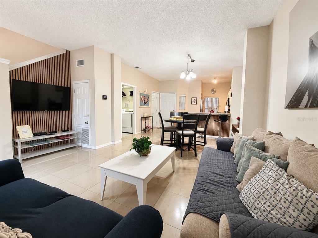 A living room with tile floors, a wood-slat accent wall, and an adjacent dining area — 4715 FLAGLER BEACH WAY, KISSIMMEE, FL