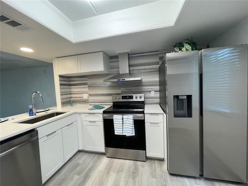 A modern kitchen features white cabinets, stainless steel appliances, and a gray-toned backsplash — 103 PALMETTO COURT UNIT 103, OLDSMAR, FL