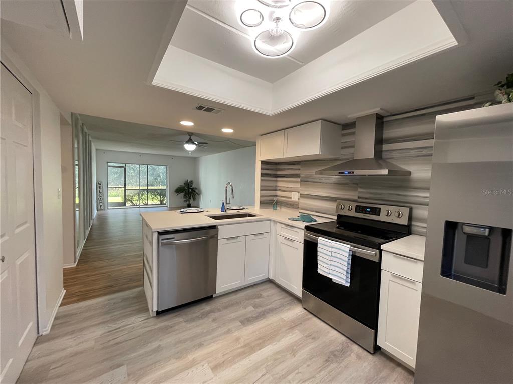 A modern kitchen features white cabinets, stainless steel appliances, and a view into the living area — 103 PALMETTO COURT UNIT 103, OLDSMAR, FL