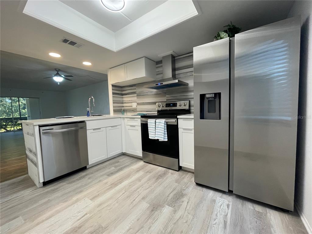 A kitchen features white cabinets, stainless steel appliances, a tiled backsplash, and light wood flooring — 103 PALMETTO COURT UNIT 103, OLDSMAR, FL