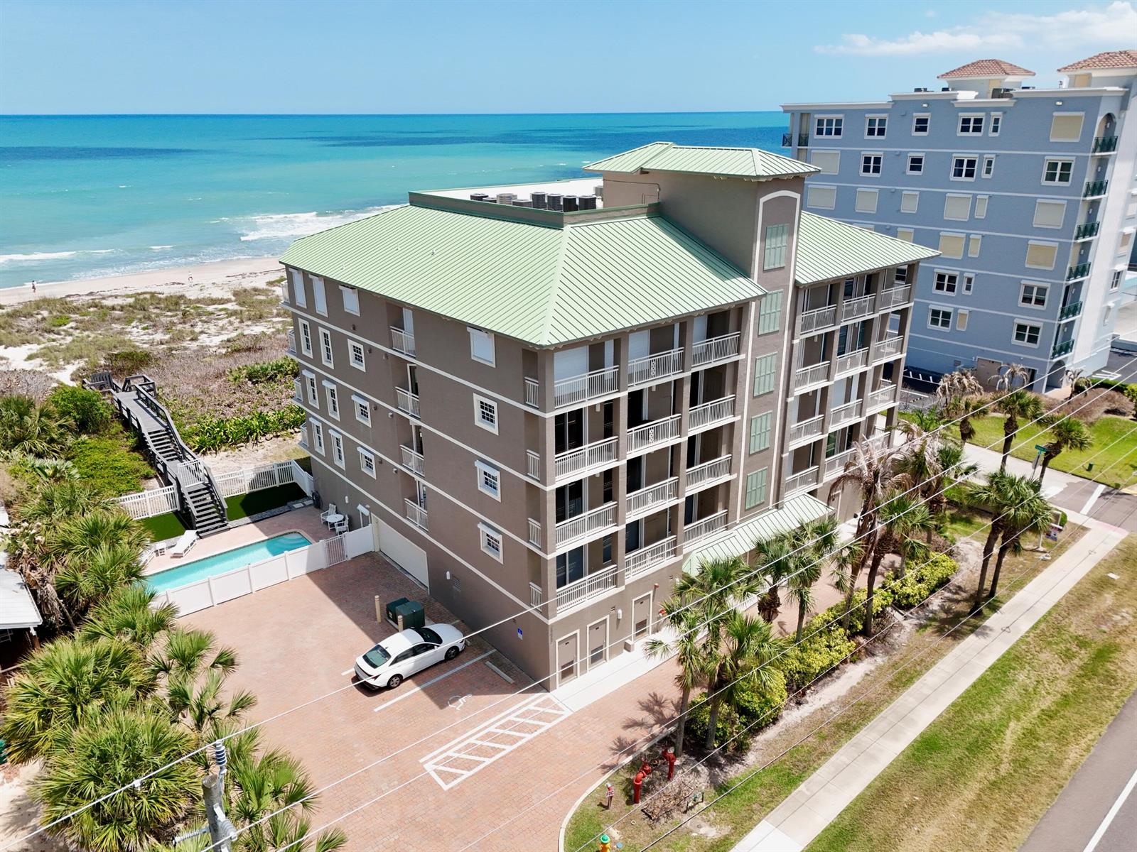An aerial view shows a multi-story tan condominium building with a green roof near the beach — 2465 S Atlantic Avenue, Cocoa Beach FL 32931, COCOA BEACH, FL