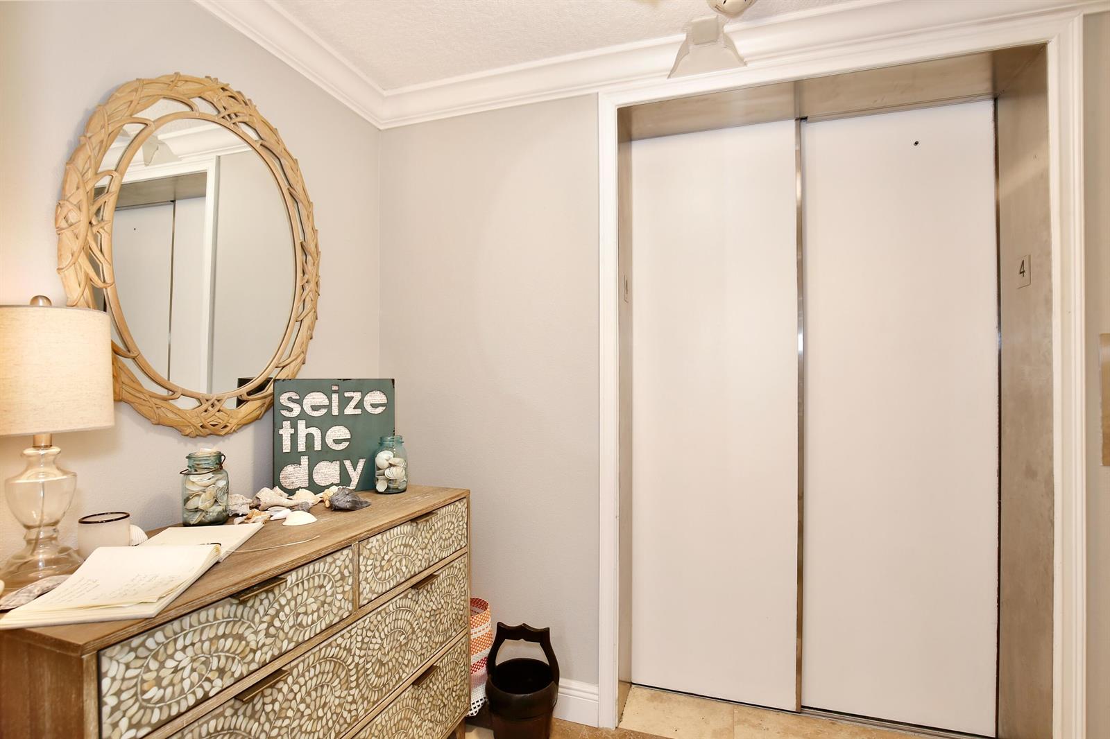A hallway features a wooden dresser with a mirror, a lamp, and an elevator door — 2465 S Atlantic Avenue, Cocoa Beach FL 32931, COCOA BEACH, FL