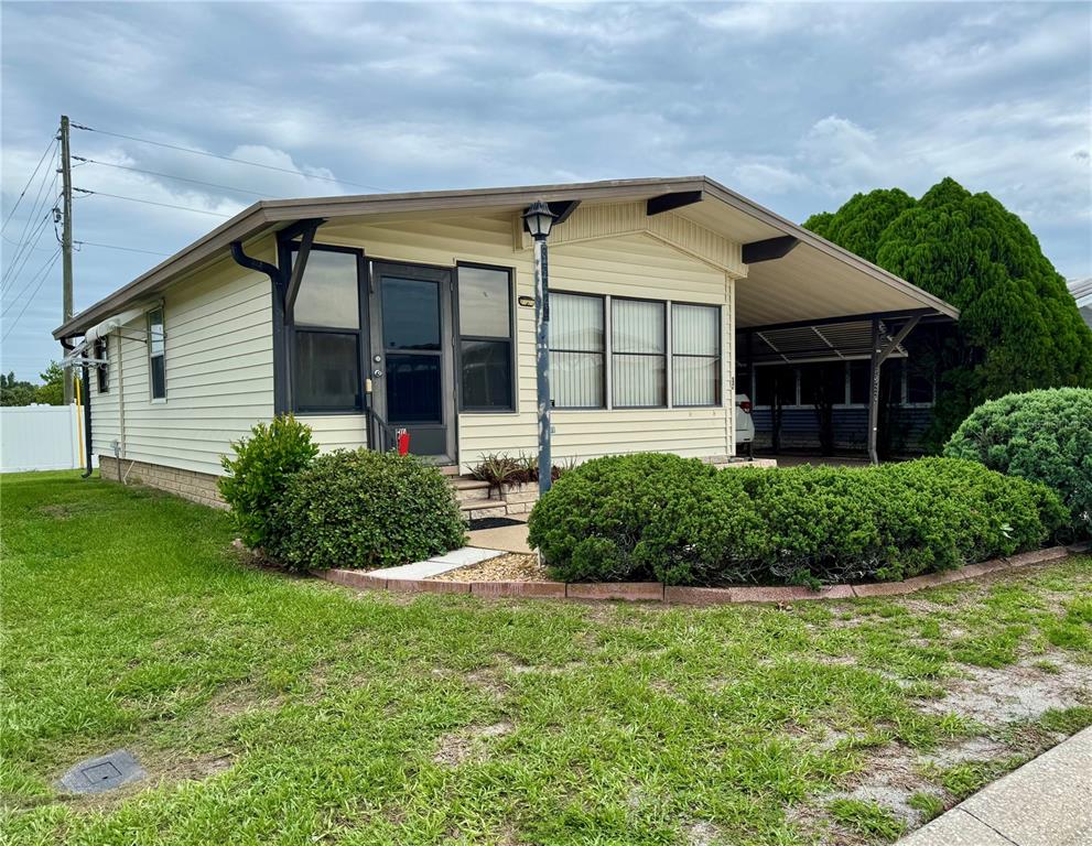 A single-story manufactured home with light siding, a carport, and a landscaped front yard — 35224 DODIE DRIVE Lot 12, ZEPHYRHILLS, FL