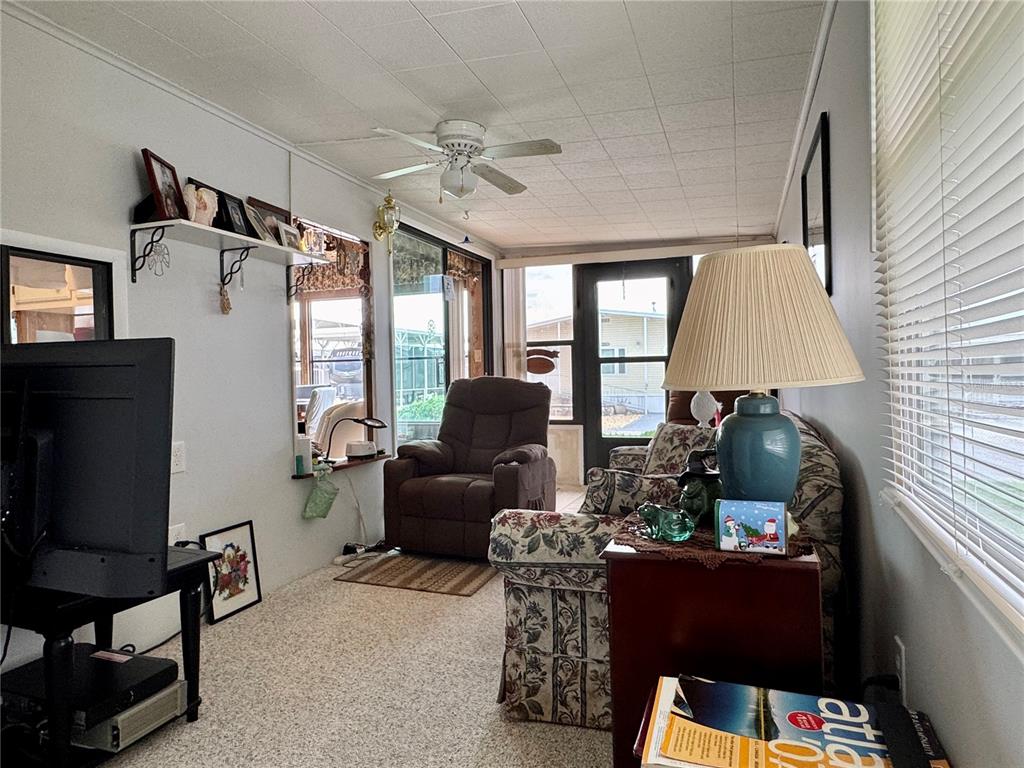 A sunroom features a floral sofa, a brown recliner, a ceiling fan, and carpeted floors — 35224 DODIE DRIVE Lot 12, ZEPHYRHILLS, FL
