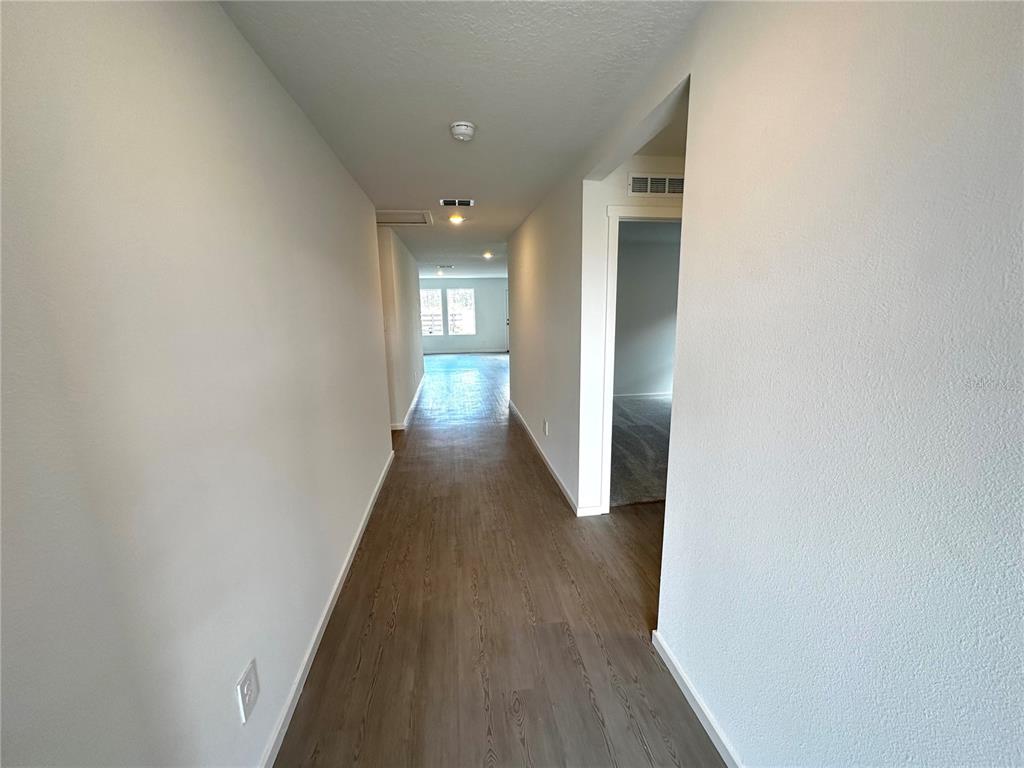 A hallway with light-colored walls and wood-look flooring leads toward a windowed room — 1975 WILDER WAY, EAGLE LAKE, FL