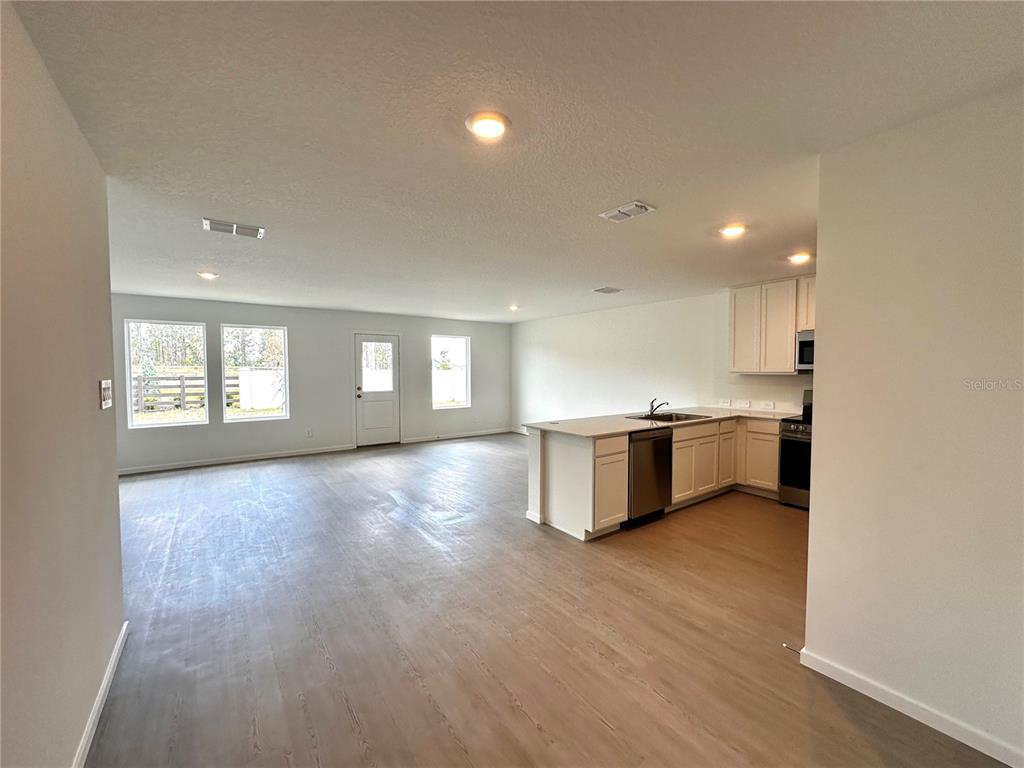 An open-concept kitchen and living area features white cabinets, stainless steel appliances, and light flooring — 1975 WILDER WAY, EAGLE LAKE, FL
