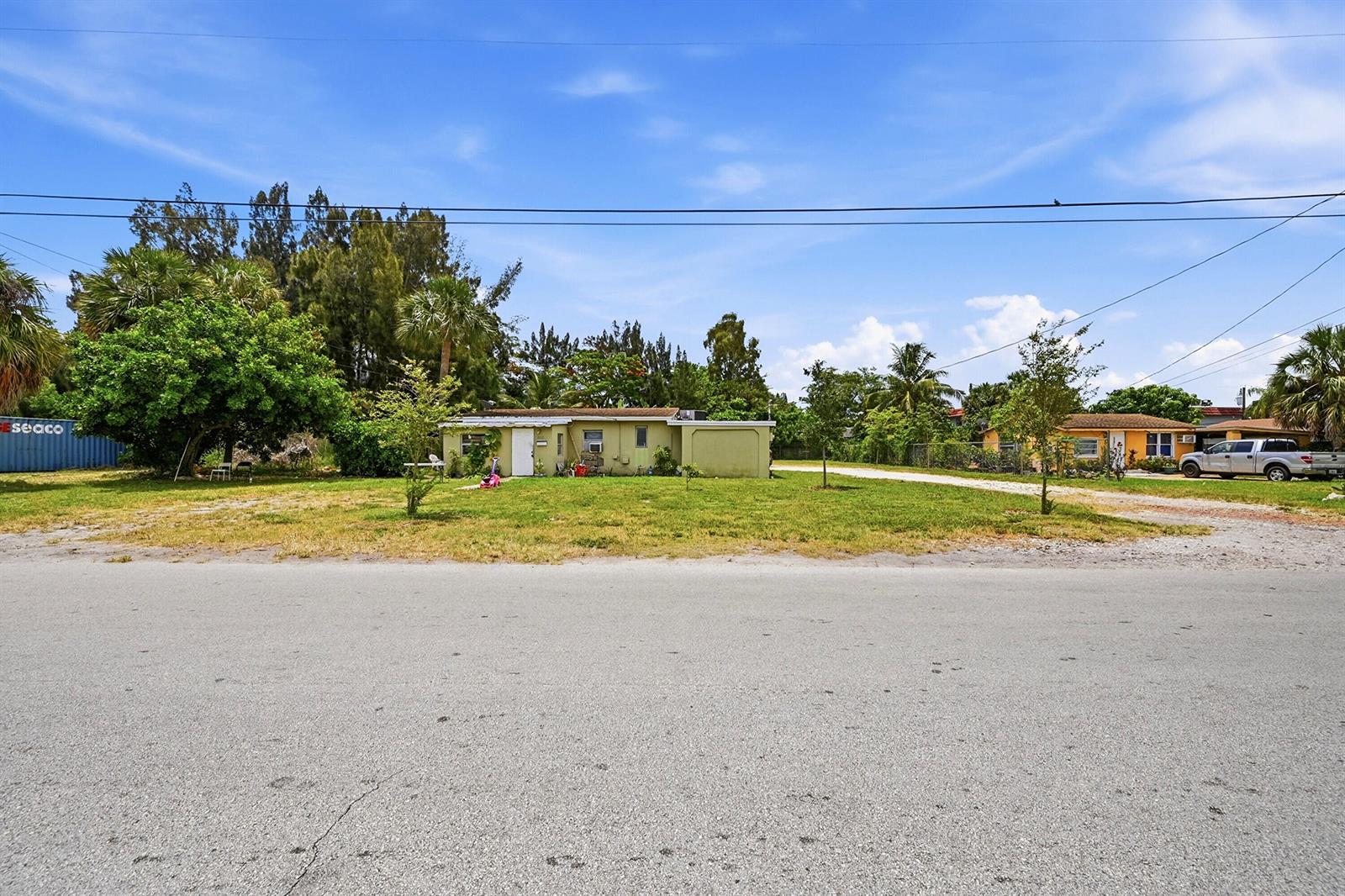 A single-story house with a large grassy yard sits under a bright blue sky — 700 SW 8th Street, Pompano Beach FL 33060, POMPANO BEACH, FL