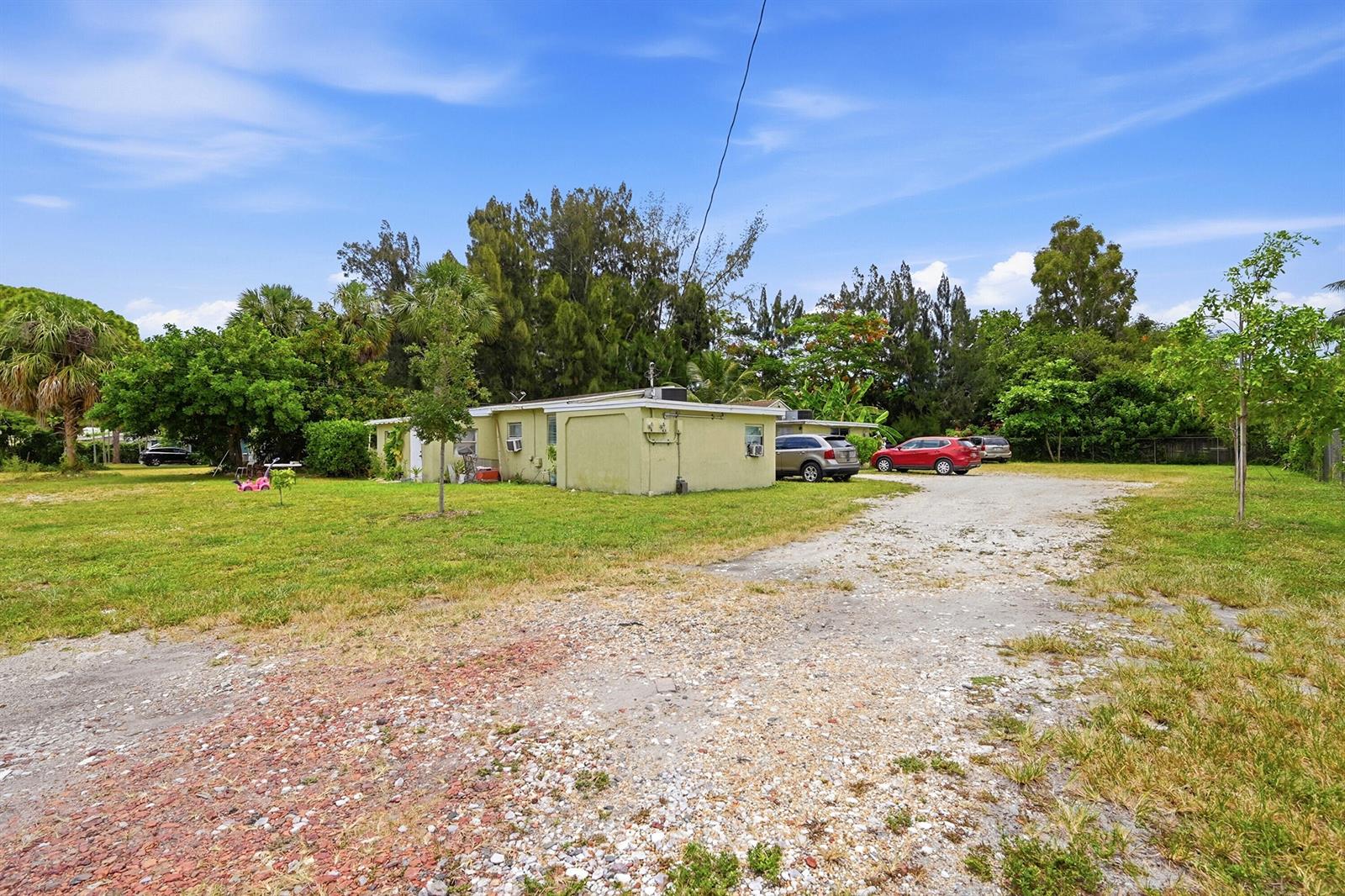 A light-colored single-story house sits on a large lot with a gravel driveway and trees — 700 SW 8th Street, Pompano Beach FL 33060, POMPANO BEACH, FL