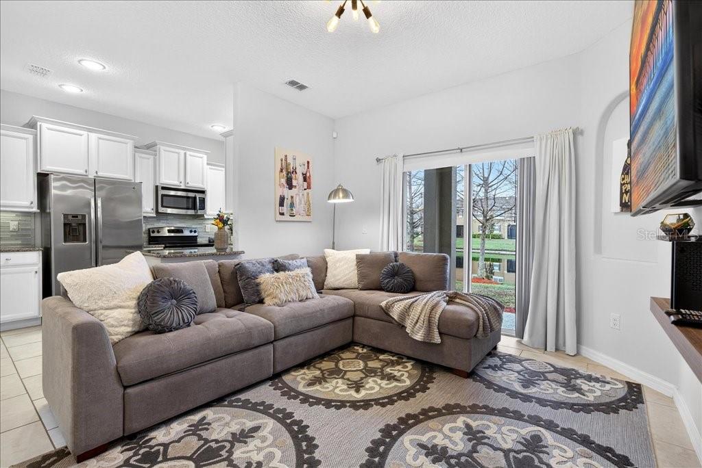 A living room with a gray sectional sofa, patterned area rug, and sliding glass doors — 165 ASTON GRANDE DRIVE, DAYTONA BEACH, FL