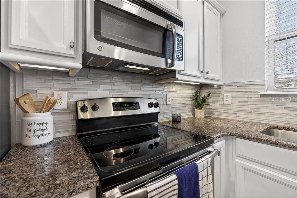 A kitchen features white cabinets, granite countertops, a stainless steel microwave, and a glass-top stove — 165 ASTON GRANDE DRIVE, DAYTONA BEACH, FL