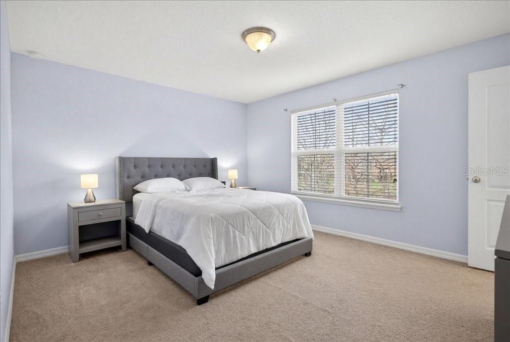 A bedroom with light blue walls, a gray upholstered bed, and a window with blinds — 165 ASTON GRANDE DRIVE, DAYTONA BEACH, FL