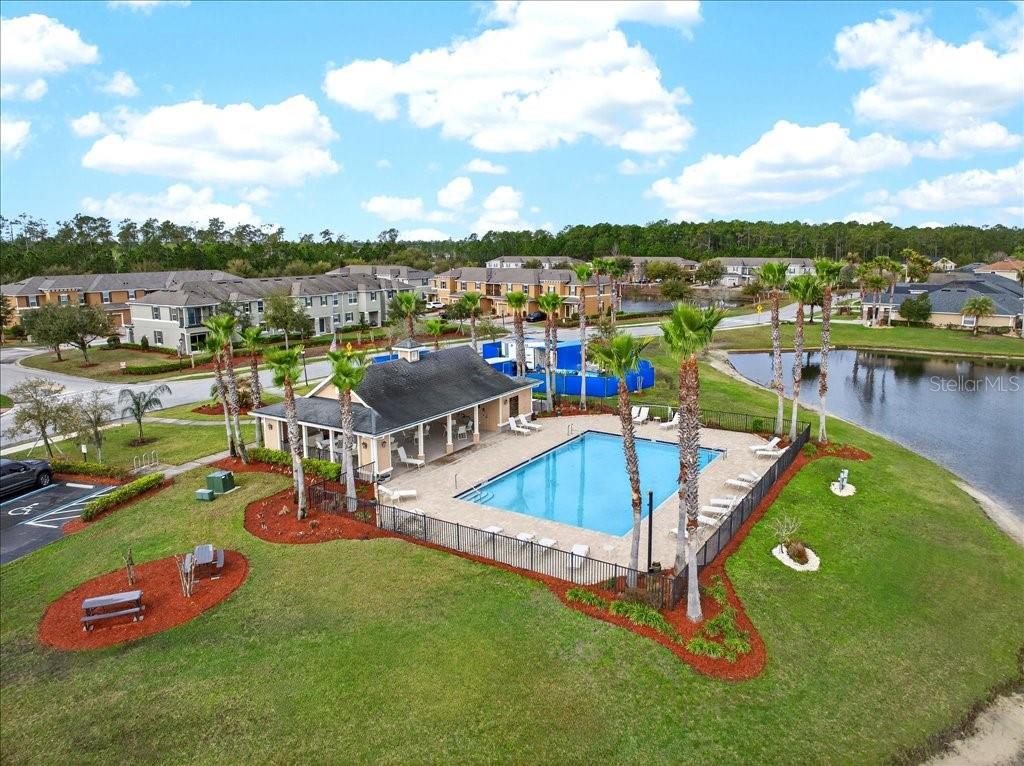 An aerial view shows a swimming pool and clubhouse surrounded by a lawn and pond — 165 ASTON GRANDE DRIVE, DAYTONA BEACH, FL