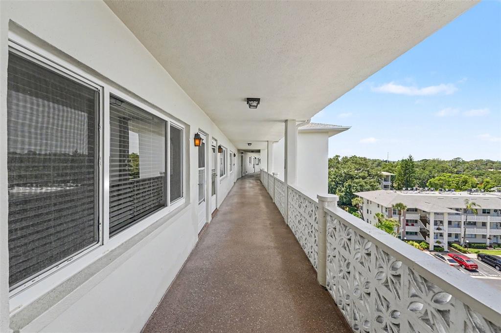 An outdoor apartment walkway features a concrete floor, white railings, and views of a parking lot — 1235 S HIGHLAND AVENUE UNIT 5-703, CLEARWATER, FL