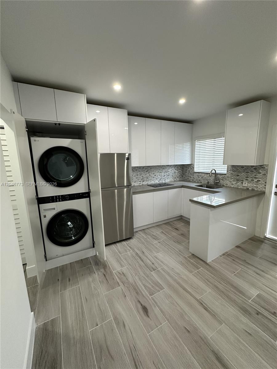 A kitchen features white cabinets, stainless steel appliances, a stacked washer-dryer, and wood-look tile flooring — 551 SW 57th Ave # 2, Miami FL 33144, MIAMI, FL