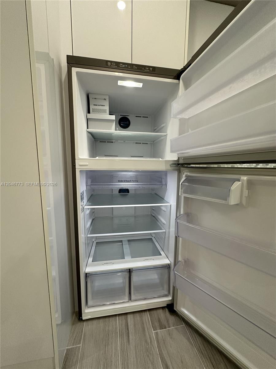 An open, empty top-freezer refrigerator stands in a kitchen with white cabinets and tiled floors — 551 SW 57th Ave # 2, Miami FL 33144, MIAMI, FL