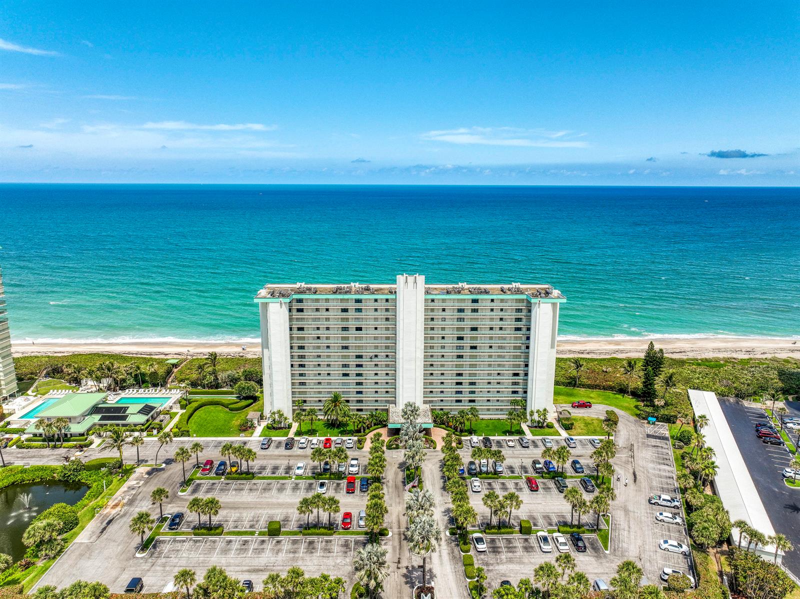An aerial view shows a tall residential building situated between a parking lot and the ocean — 9940 S Ocean Drive # G5, Jensen Beach FL 34957, JENSEN BEACH, FL