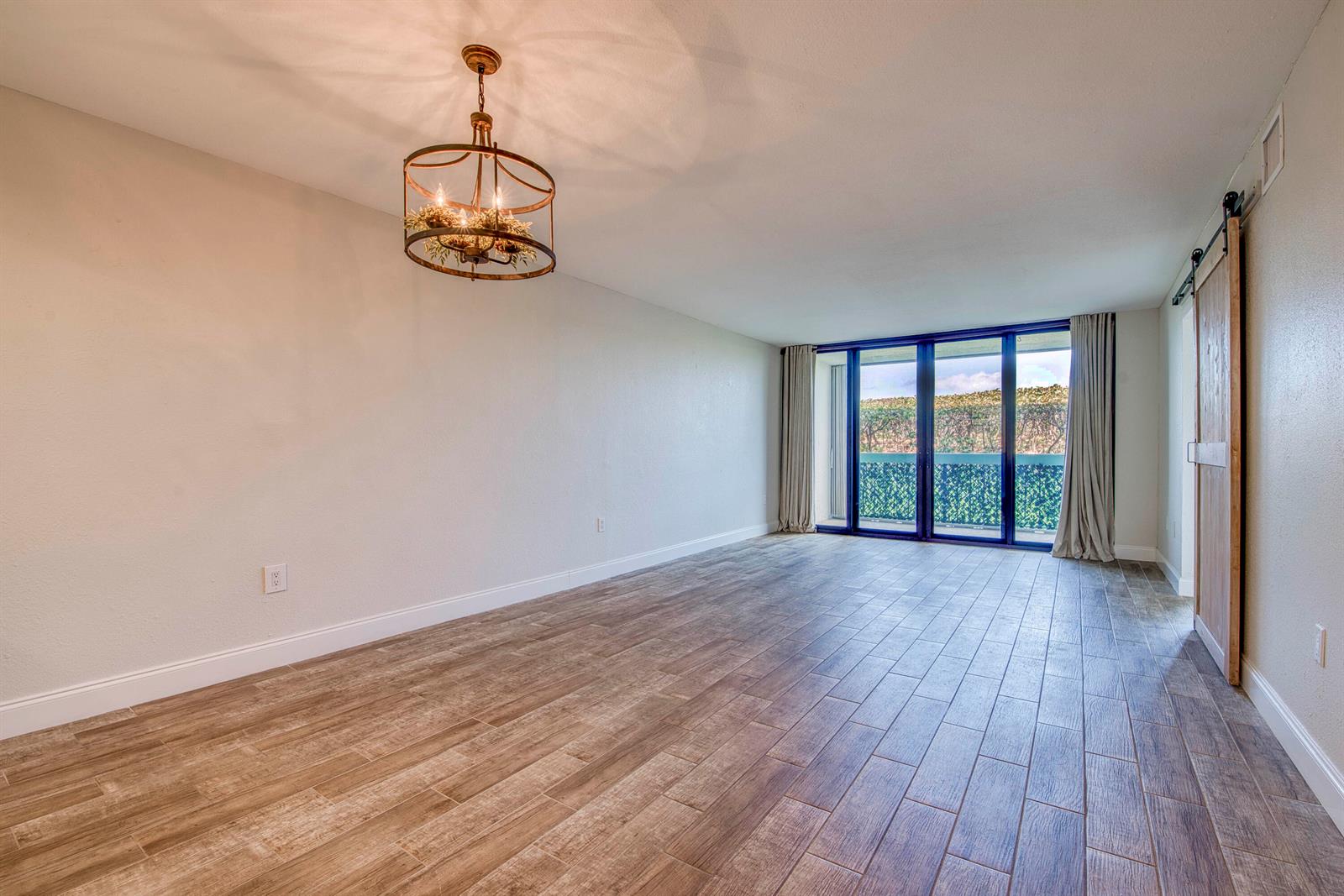 An empty room features wood-look tile flooring, a rustic chandelier, and sliding glass balcony doors — 9940 S Ocean Drive # G5, Jensen Beach FL 34957, JENSEN BEACH, FL