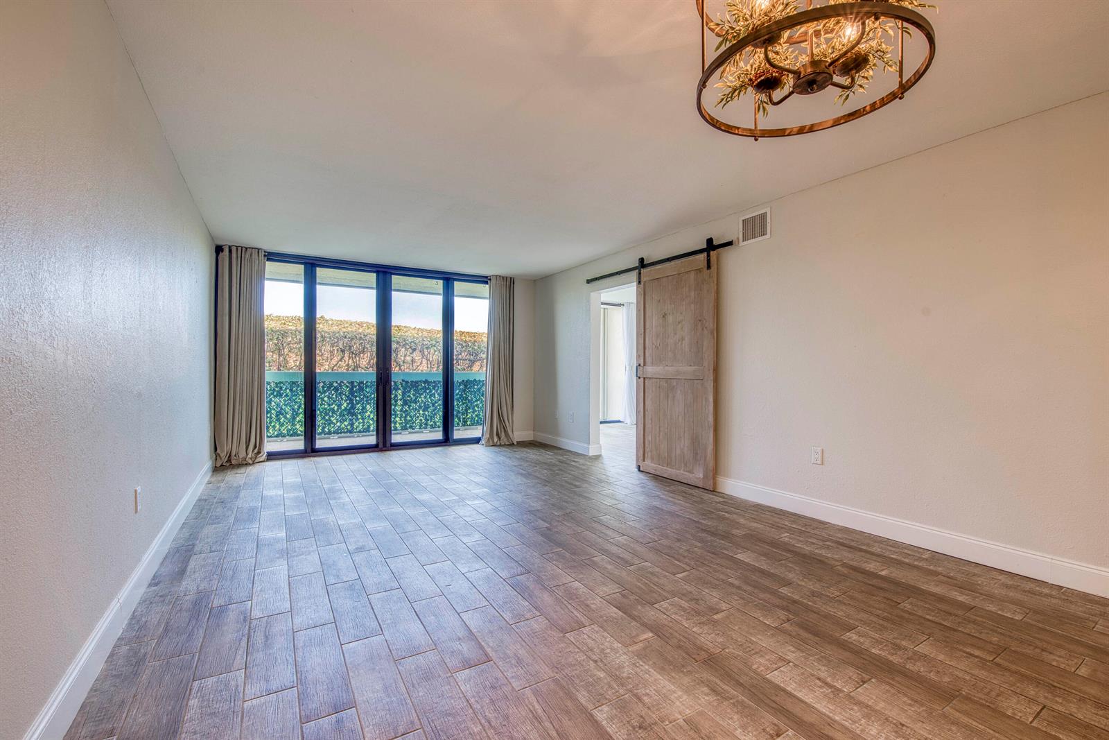 An empty room features wood-look tile flooring, a rustic barn door, and large glass doors — 9940 S Ocean Drive # G5, Jensen Beach FL 34957, JENSEN BEACH, FL