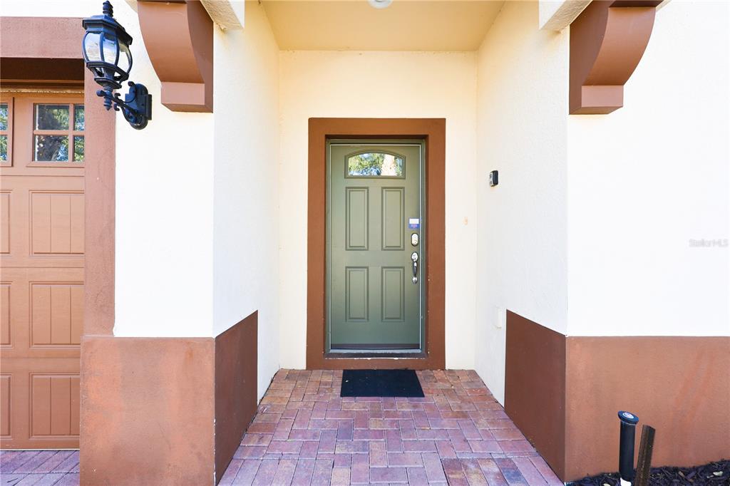 A green front door with a small window sits under a covered entryway with brick pavers — 8812 MACAPA DRIVE, KISSIMMEE, FL