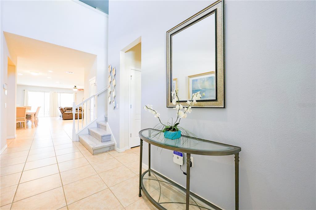 A foyer features a glass-topped console table, a wall mirror, and stairs leading to a loft — 8812 MACAPA DRIVE, KISSIMMEE, FL