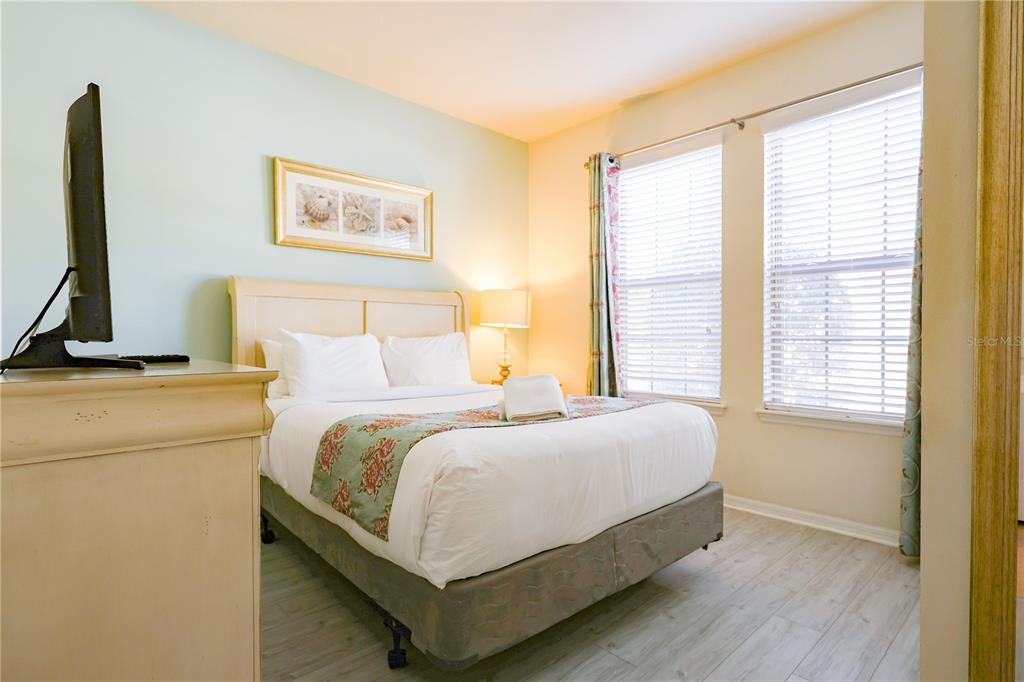 A bedroom features a queen bed, a television on a dresser, and two windows — 8812 MACAPA DRIVE, KISSIMMEE, FL