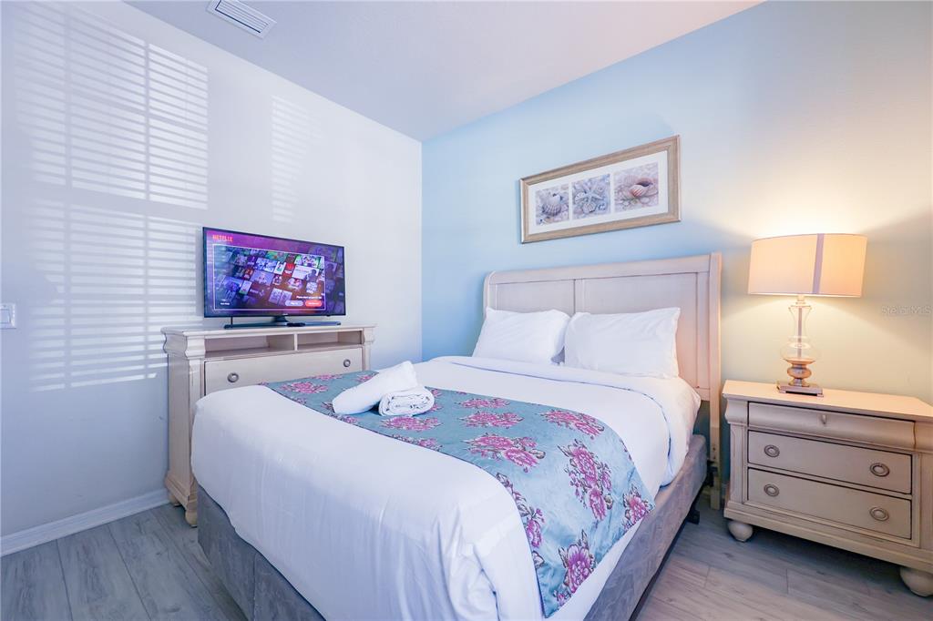 A bedroom features a bed with a floral runner, a television on a dresser, and lamp — 8812 MACAPA DRIVE, KISSIMMEE, FL