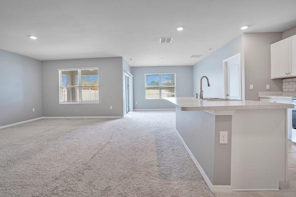 A carpeted living area opens to a kitchen with a breakfast bar and white cabinets — 2636 NEVERLAND DRIVE, NEW SMYRNA BEACH, FL