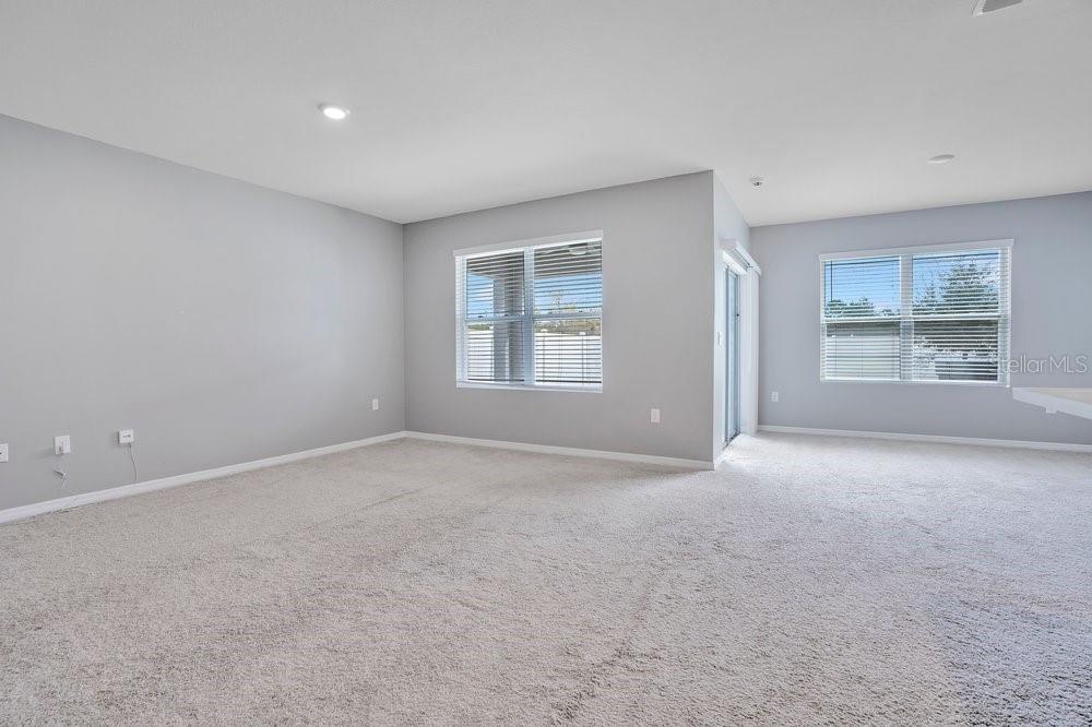 An empty living room with gray walls, beige carpeting, and two windows — 2636 NEVERLAND DRIVE, NEW SMYRNA BEACH, FL