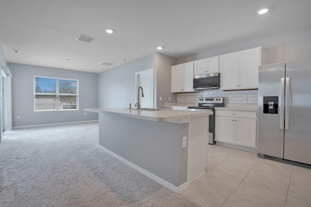 A kitchen with white cabinets, stainless steel appliances, and an island overlooks a carpeted room — 2636 NEVERLAND DRIVE, NEW SMYRNA BEACH, FL