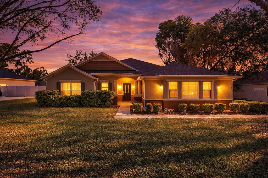 A single-story house with a tan exterior and a sunset sky in the background — 2613 BREEZY MEADOW ROAD, APOPKA, FL