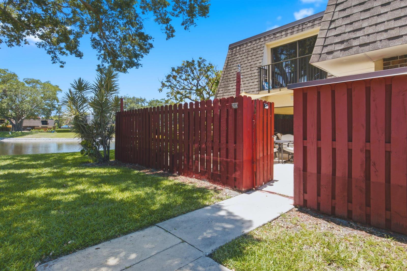 A red wooden fence encloses a patio area next to a building near a pond — 2883 SW 22nd Circle # 51a, Delray Beach FL 33445, DELRAY BEACH, FL