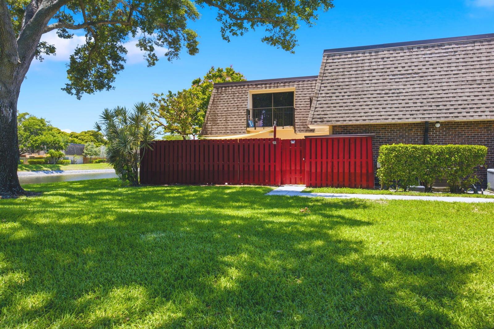 A red wooden fence encloses a patio area in front of a two-story brick townhouse — 2883 SW 22nd Circle # 51a, Delray Beach FL 33445, DELRAY BEACH, FL